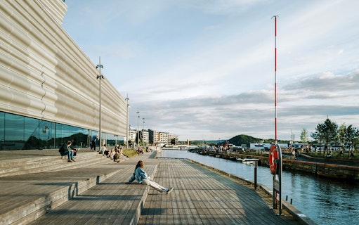 People relaxing on the wooden steps outside the Munch Museum in Oslo, with a view of the waterfront.