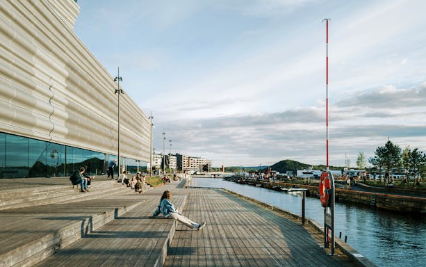 People relaxing on the wooden steps outside the Munch Museum in Oslo, with a view of the waterfront.