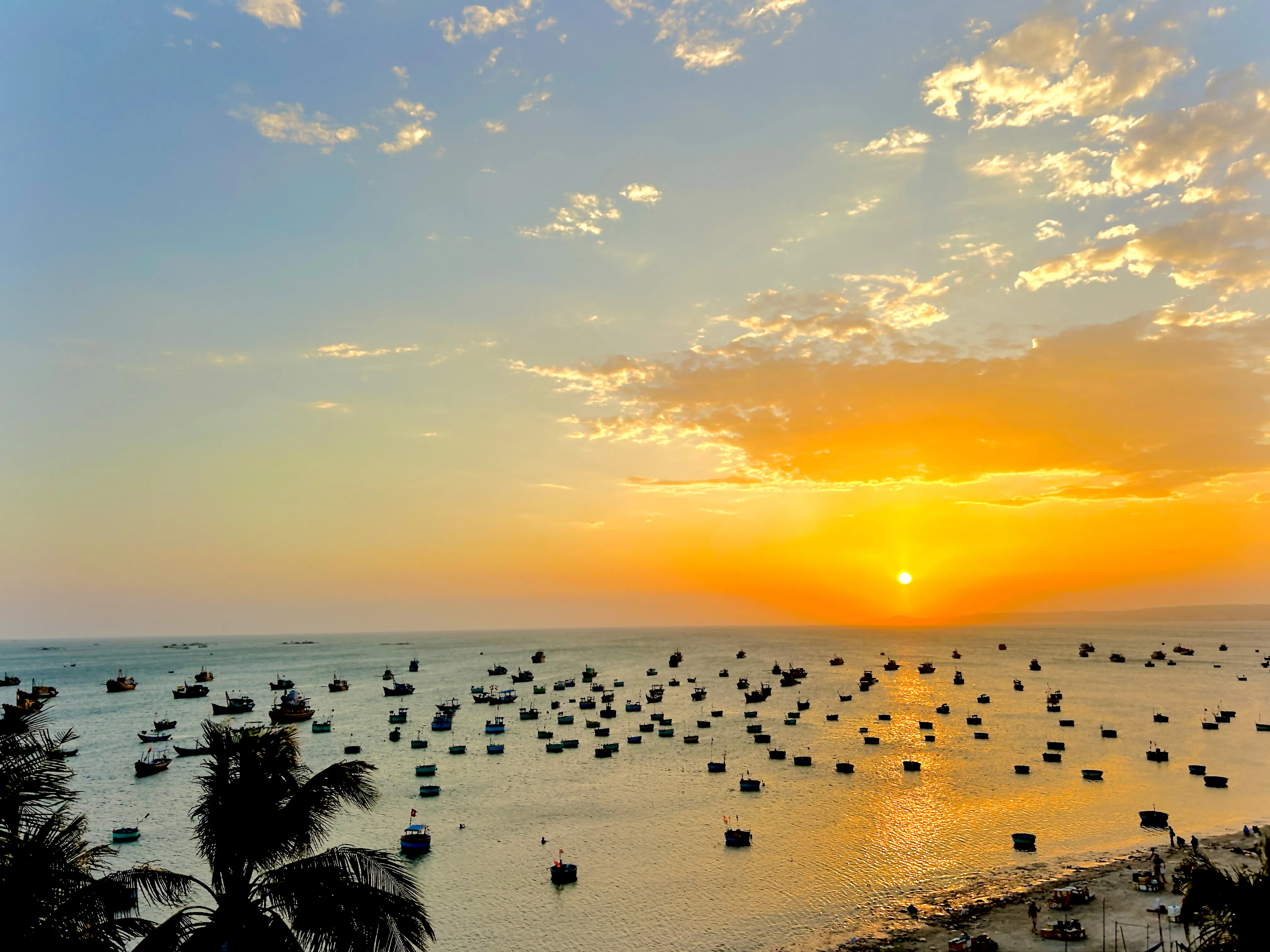 Boats on the water at sunset in Mui Ne, Vietnam, viewed from the shore.