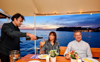 Couple enjoying drinks on Dubrovnik sunset cruise with waiter pouring wine.