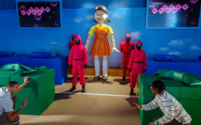 Participants reenact Squid Game scene with giant doll and guards at Netflix house in Dallas.