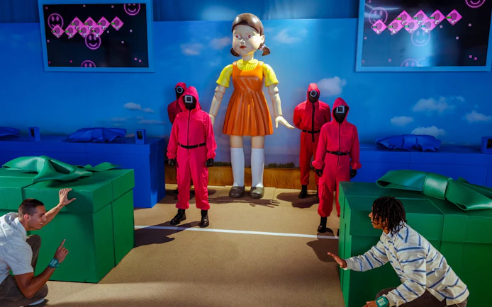Participants reenact Squid Game scene with giant doll and guards at Netflix house in Dallas.