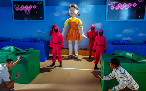 Participants reenact Squid Game scene with giant doll and guards at Netflix house in Dallas.