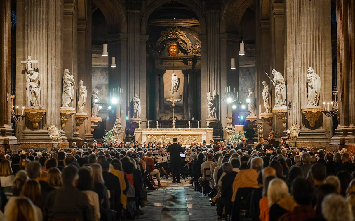Orchestra performing in St Sulpice Church, Paris, with audience seated in the nave.