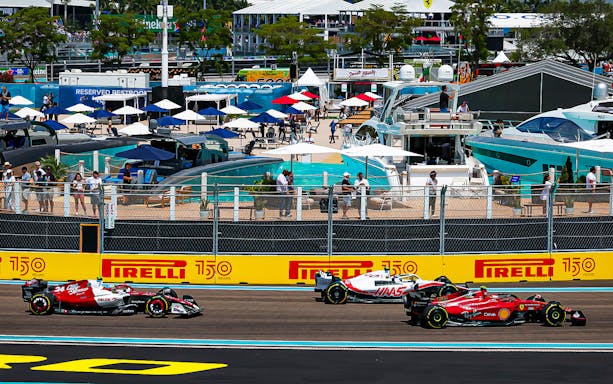 Race cars on track at Formula 1 Miami Grand Prix with yachts and spectators in background.