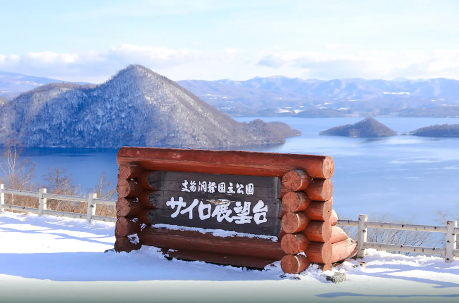 Noboribetsu Hell Valley sign with snowy Lake Toya and Mt. Usu in Hokkaido background.