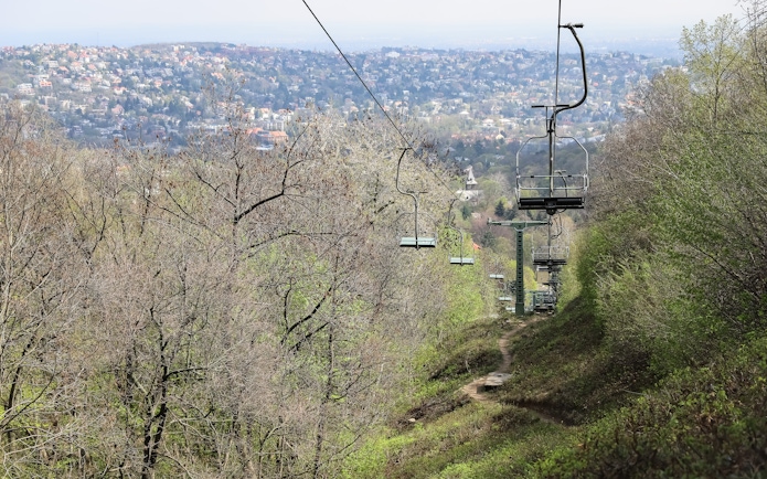 Chairlift ascending over a forested hillside with a cityscape in the background.