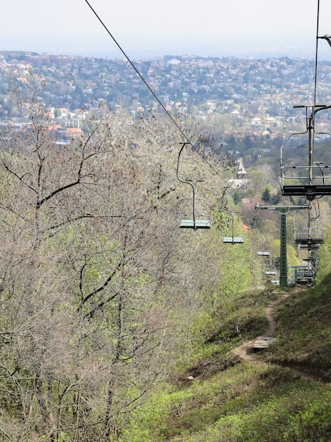 Chairlift ascending over a forested hillside with a cityscape in the background.