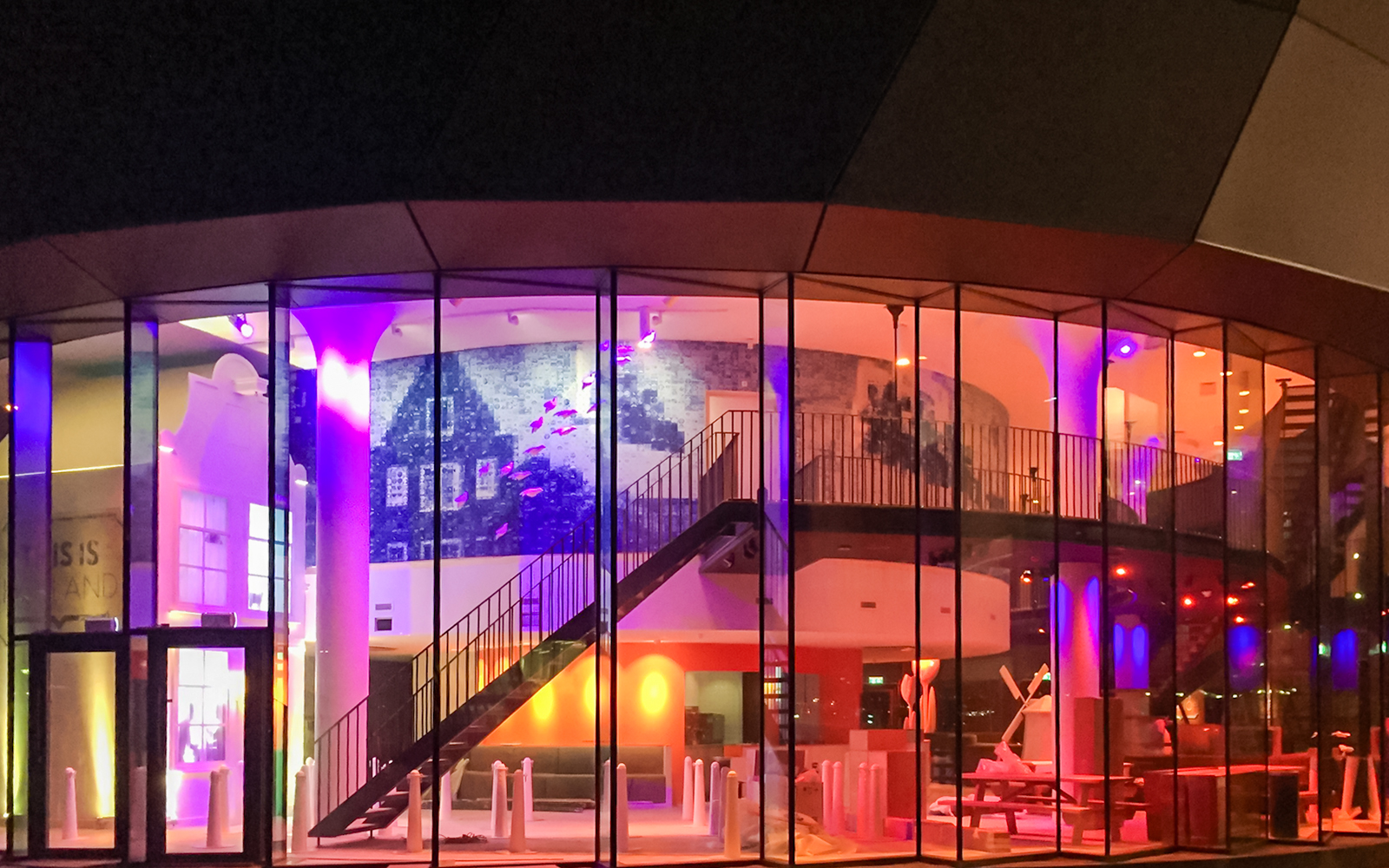 Exteriors of This is Holland with colorful illuminated glass facade and interior staircase.