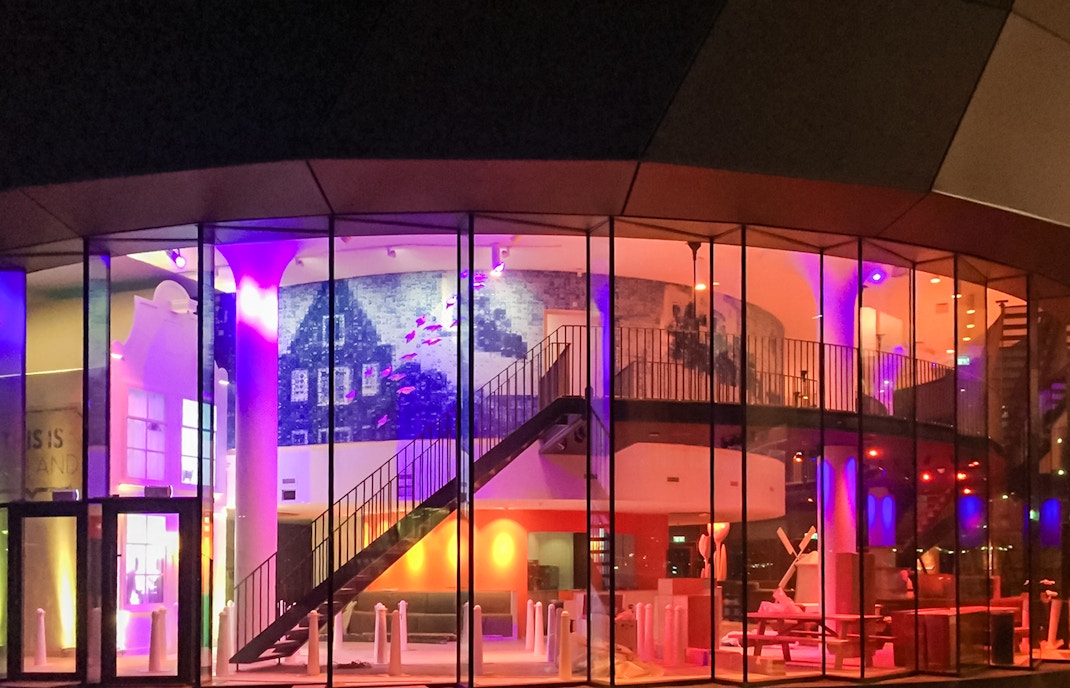Exteriors of This is Holland with colorful illuminated glass facade and interior staircase.