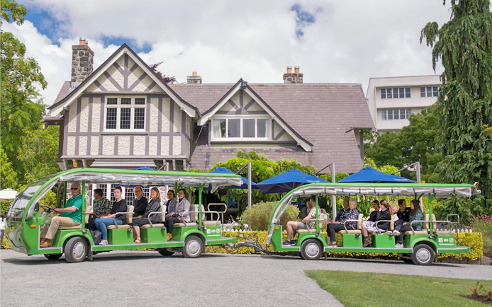 Tour group on electric tram at Botanic Gardens, Christchurch, with historic building in background.