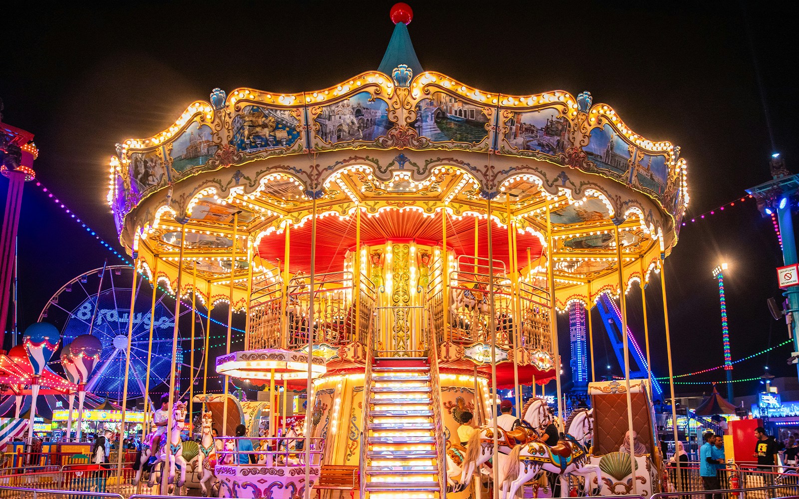 Carousel at night in Global Village Dubai with colorful lights and people enjoying the ride.