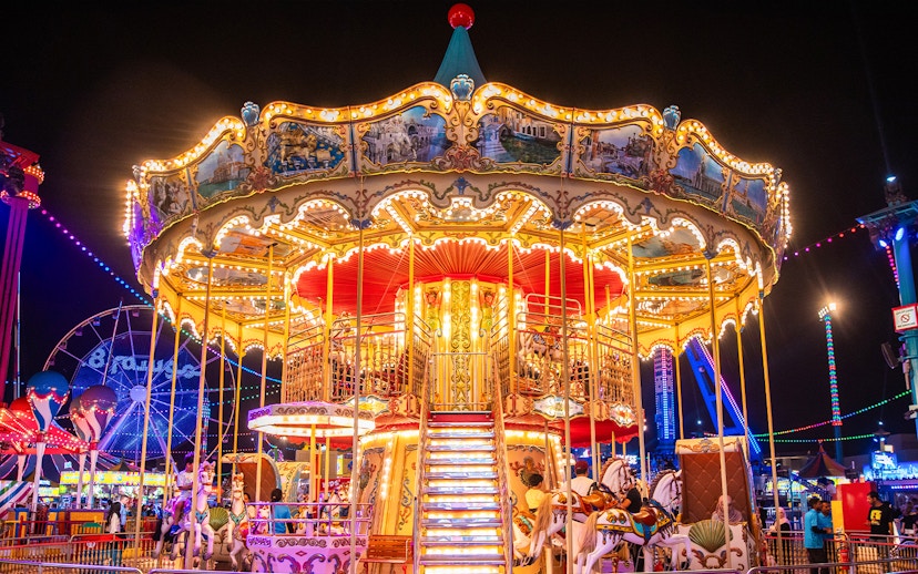 Carousel at night in Global Village Dubai with colorful lights and people enjoying the ride.