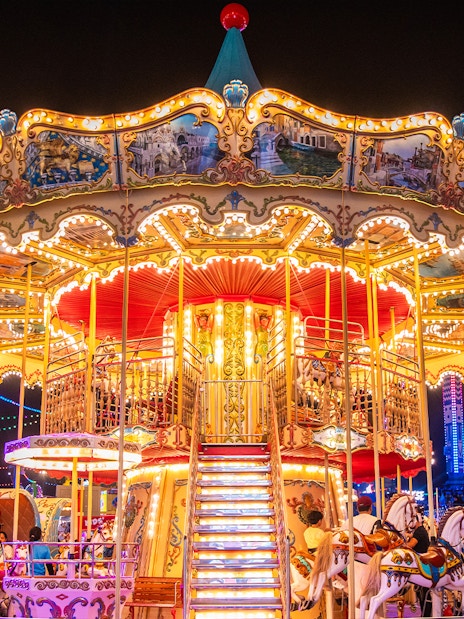 Carousel at night in Global Village Dubai with colorful lights and people enjoying the ride.