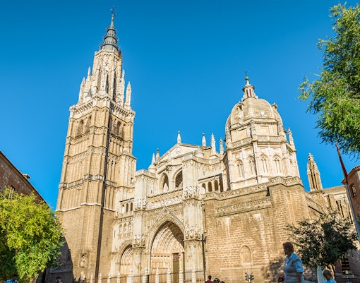 Toledo Cathedral facade with bell tower under clear blue sky, Spain.