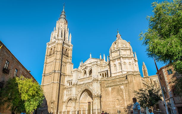 Toledo Cathedral facade with bell tower under clear blue sky, Spain.