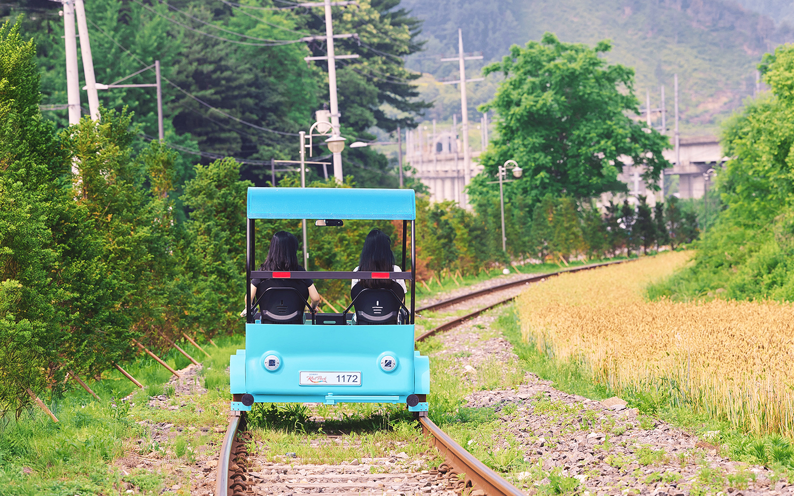 Two people riding a blue rail bike on tracks through countryside near Gapyeong, South Korea.