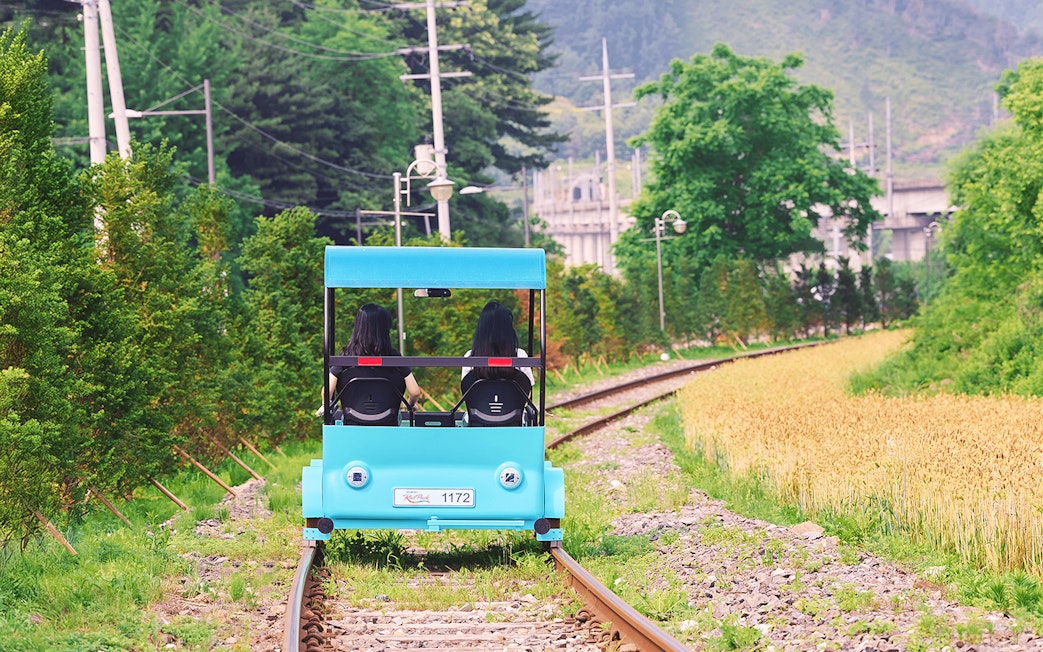 Two people riding a blue rail bike on tracks through countryside near Gapyeong, South Korea.