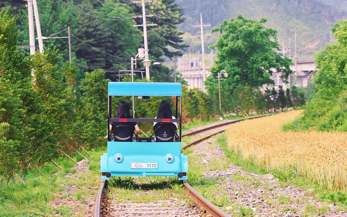 Two people riding a blue rail bike on tracks through countryside near Gapyeong, South Korea.