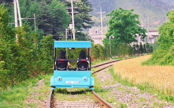 Two people riding a blue rail bike on tracks through countryside near Gapyeong, South Korea.