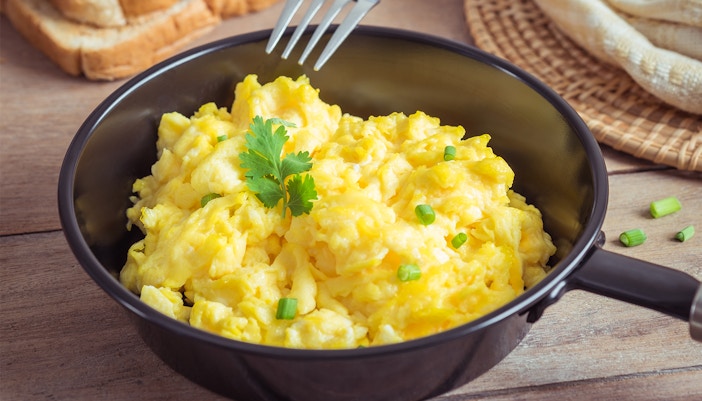 Scrambled egg in frying pan and toast on wooden table