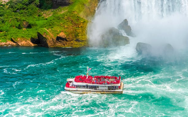 Boat approaching Niagara Falls surrounded by mist and turquoise water.