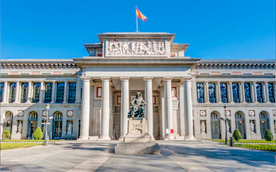 Prado Museum entrance in Madrid with statue and visitors nearby.