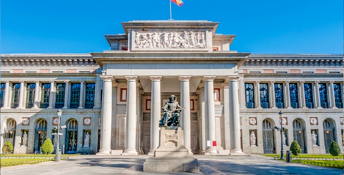 Prado Museum entrance in Madrid with statue and visitors nearby.