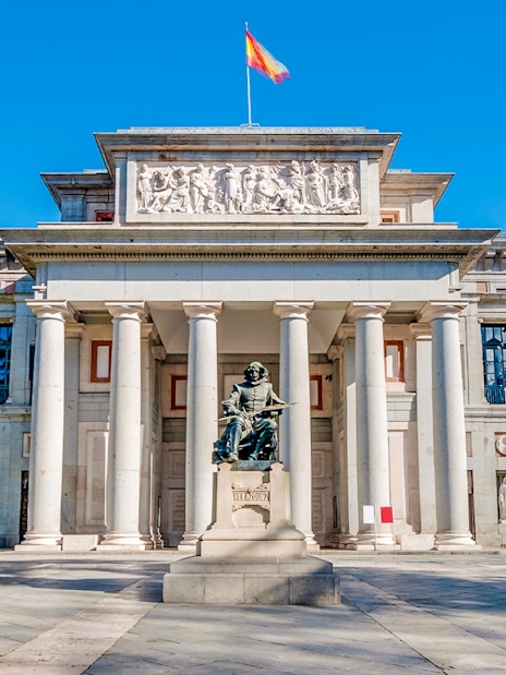 Prado Museum entrance in Madrid with statue and visitors nearby.