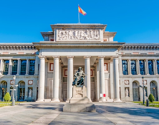 Prado Museum entrance in Madrid with visitors and a HOHO bus in the background.