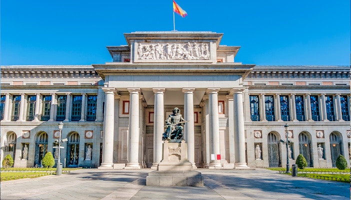 Prado Museum entrance in Madrid with visitors and a HOHO bus in the background.