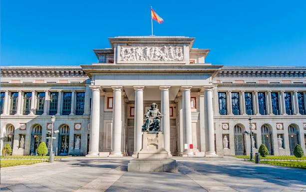 Prado Museum entrance in Madrid with statue and visitors nearby.