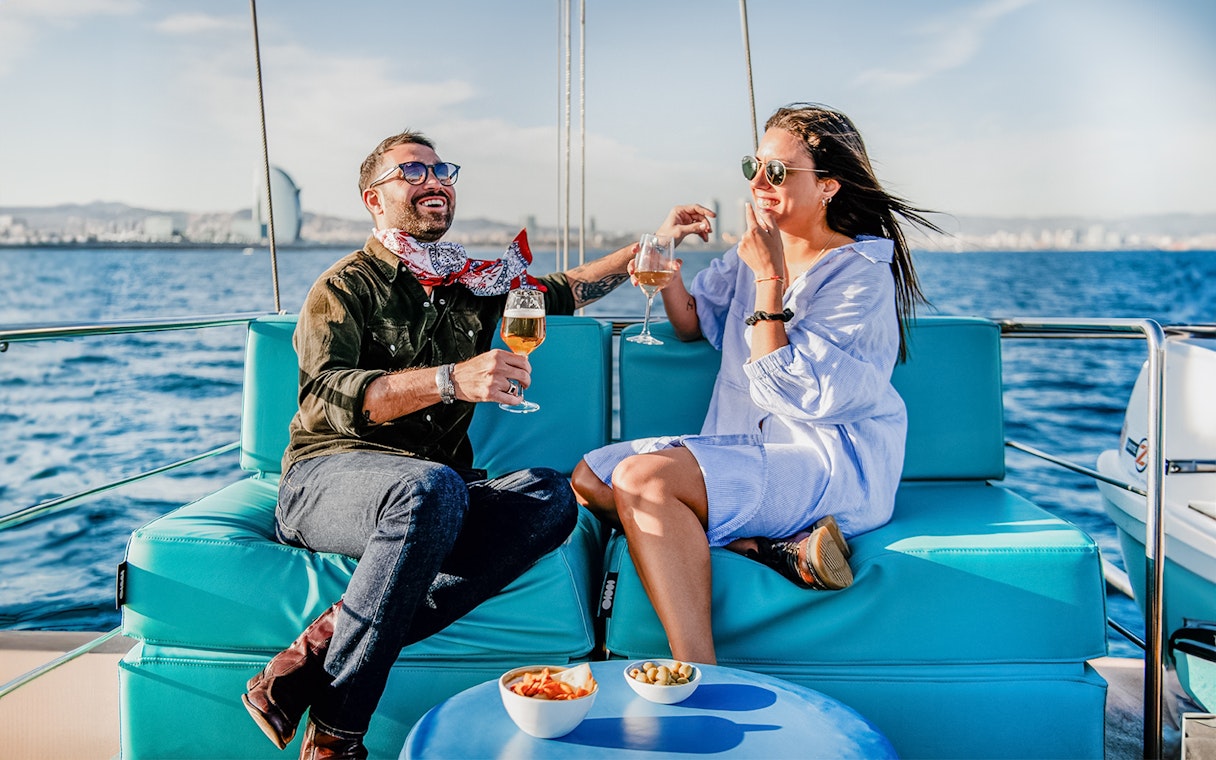 Couple enjoying drinks on a catamaran with Barcelona skyline in the background.