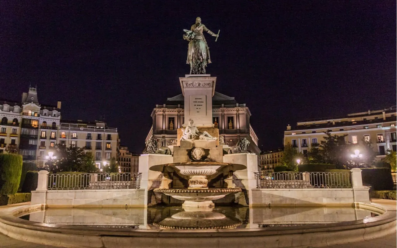 Statue and fountain at Plaza de Oriente, Madrid, illuminated at night.
