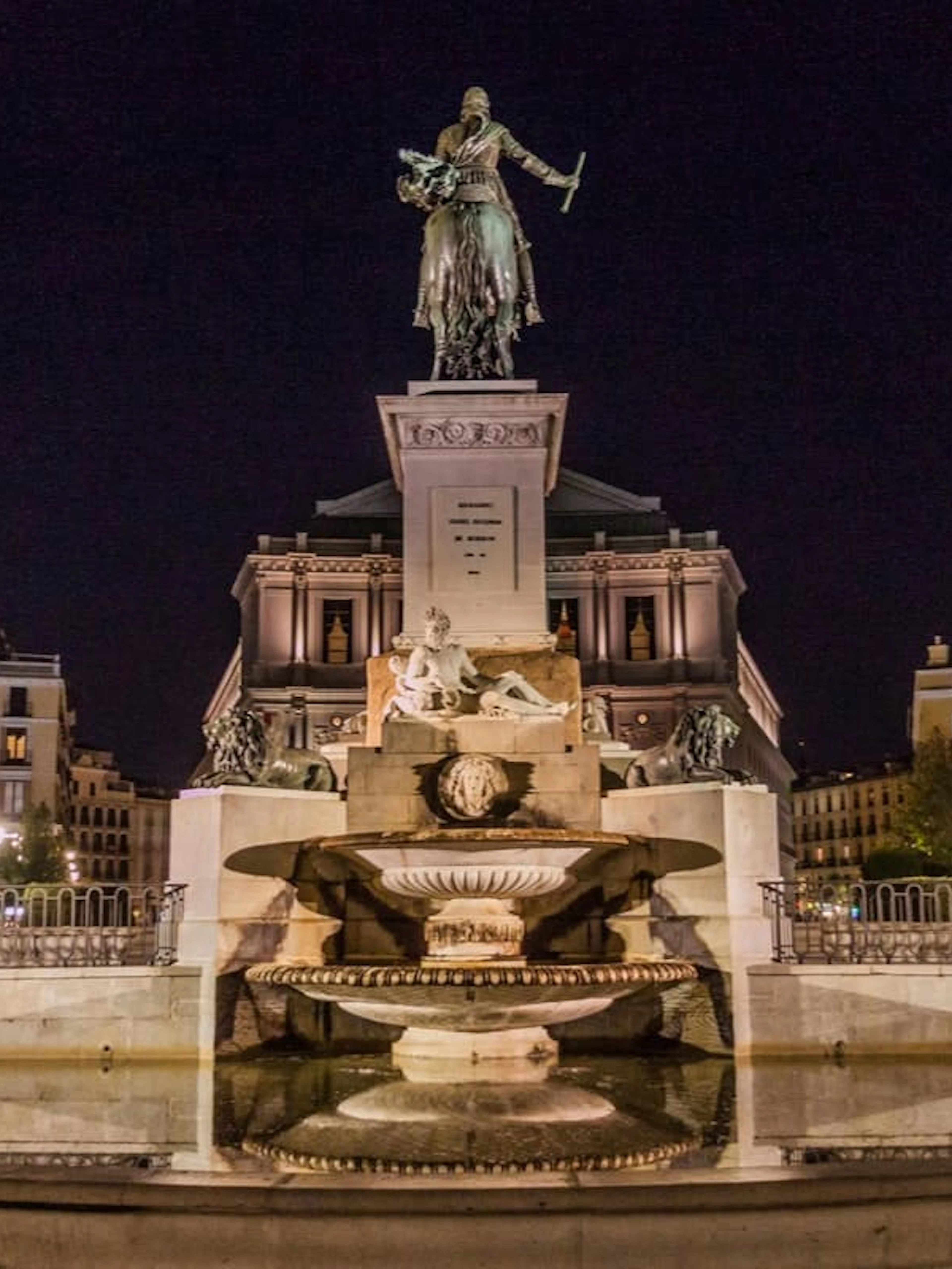 Statue and fountain at Plaza de Oriente, Madrid, illuminated at night.