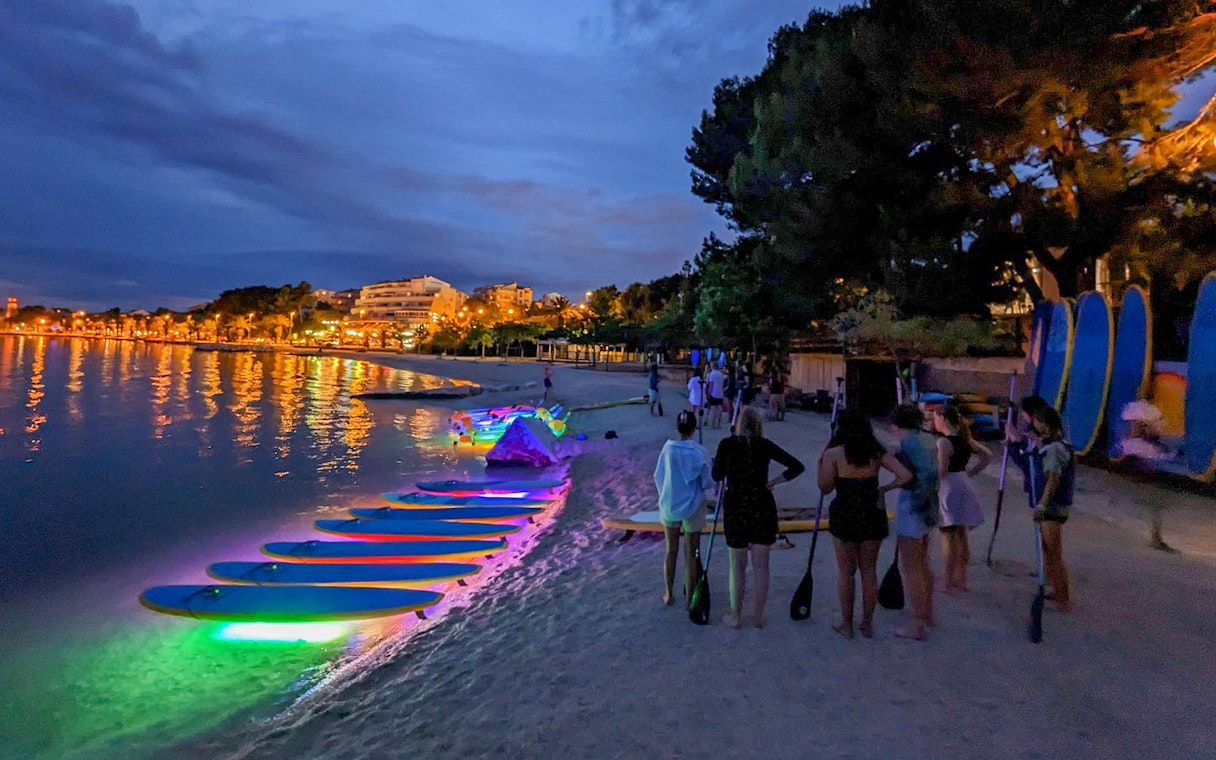 Paddleboards with glowing lights on a beach at night, SUP Glow Tour in Split.
