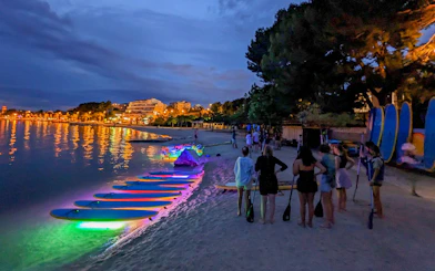 Paddleboards with glowing lights on a beach at night, SUP Glow Tour in Split.
