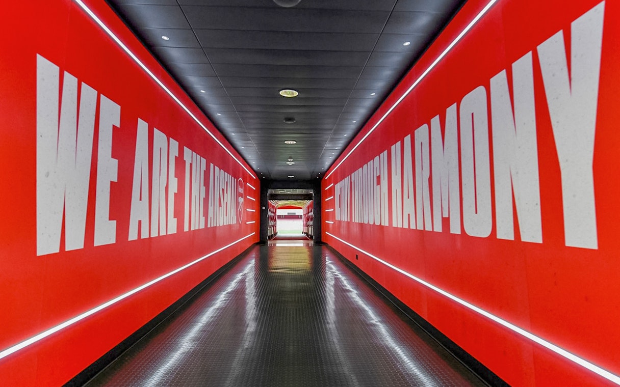 Arsenal FC Emirates Stadium tunnel with red walls and motivational text.