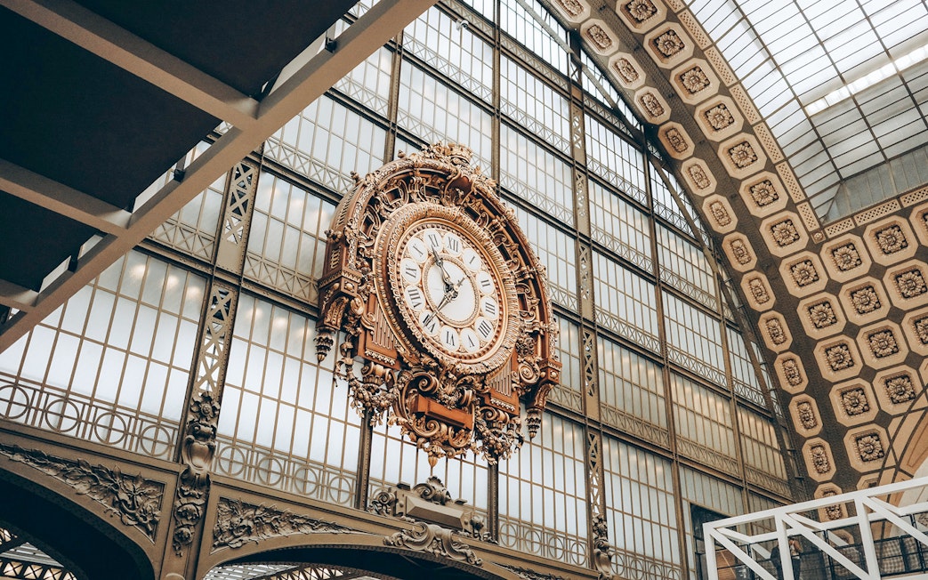 Ornate clock inside Orsay Museum, Paris, with glass ceiling background.