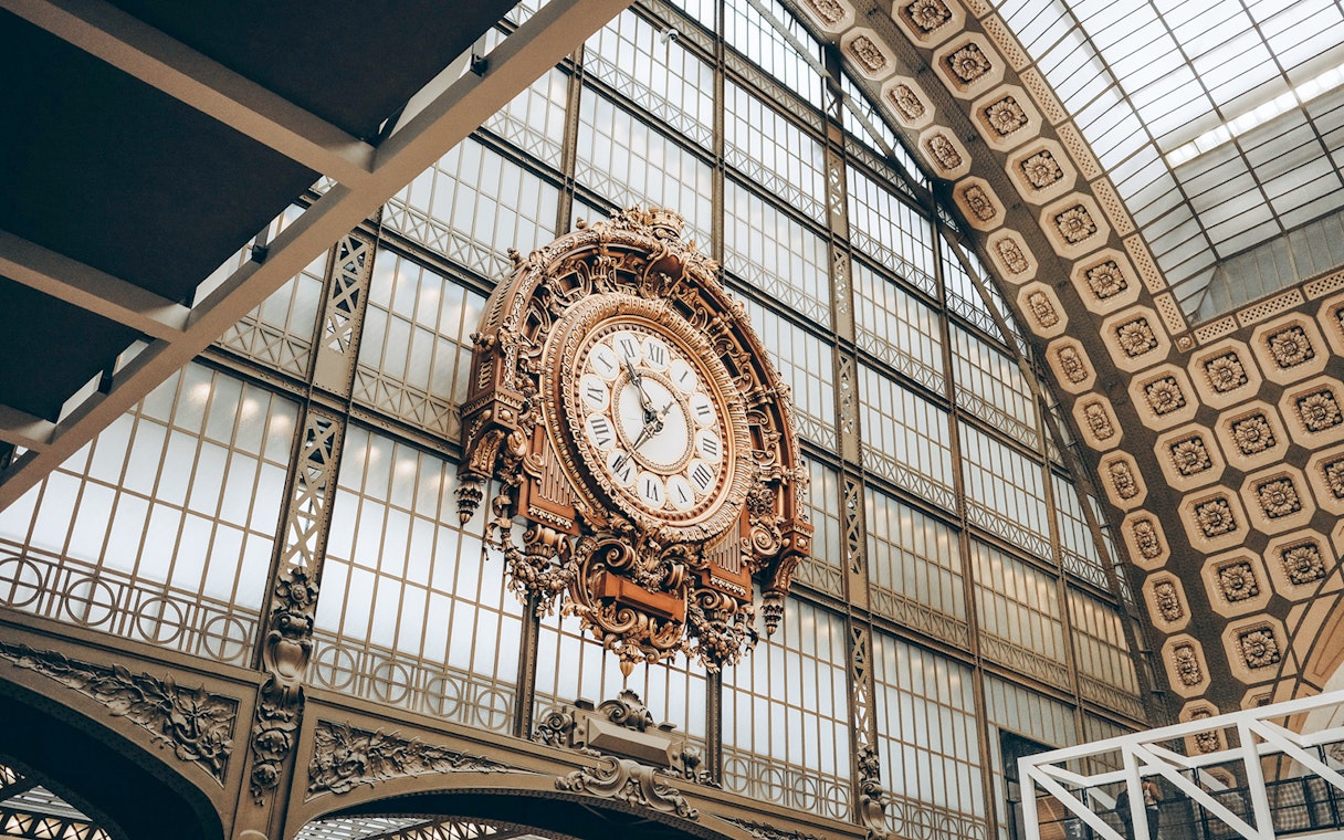 Ornate clock inside Orsay Museum, Paris, with glass ceiling background.