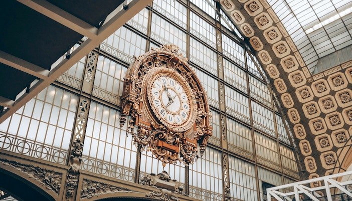 Ornate clock inside Orsay Museum, Paris, with glass ceiling background.