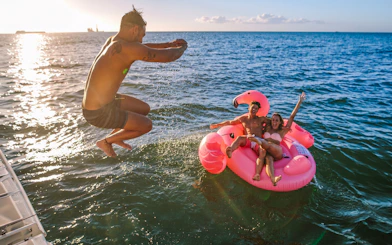 Man jumping into the sea near a pink flamingo float with two people on a Heraklion catamaran cruise.