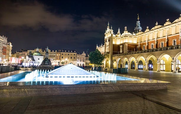 Krakow's Main Square at night with illuminated Cloth Hall and fountain.
