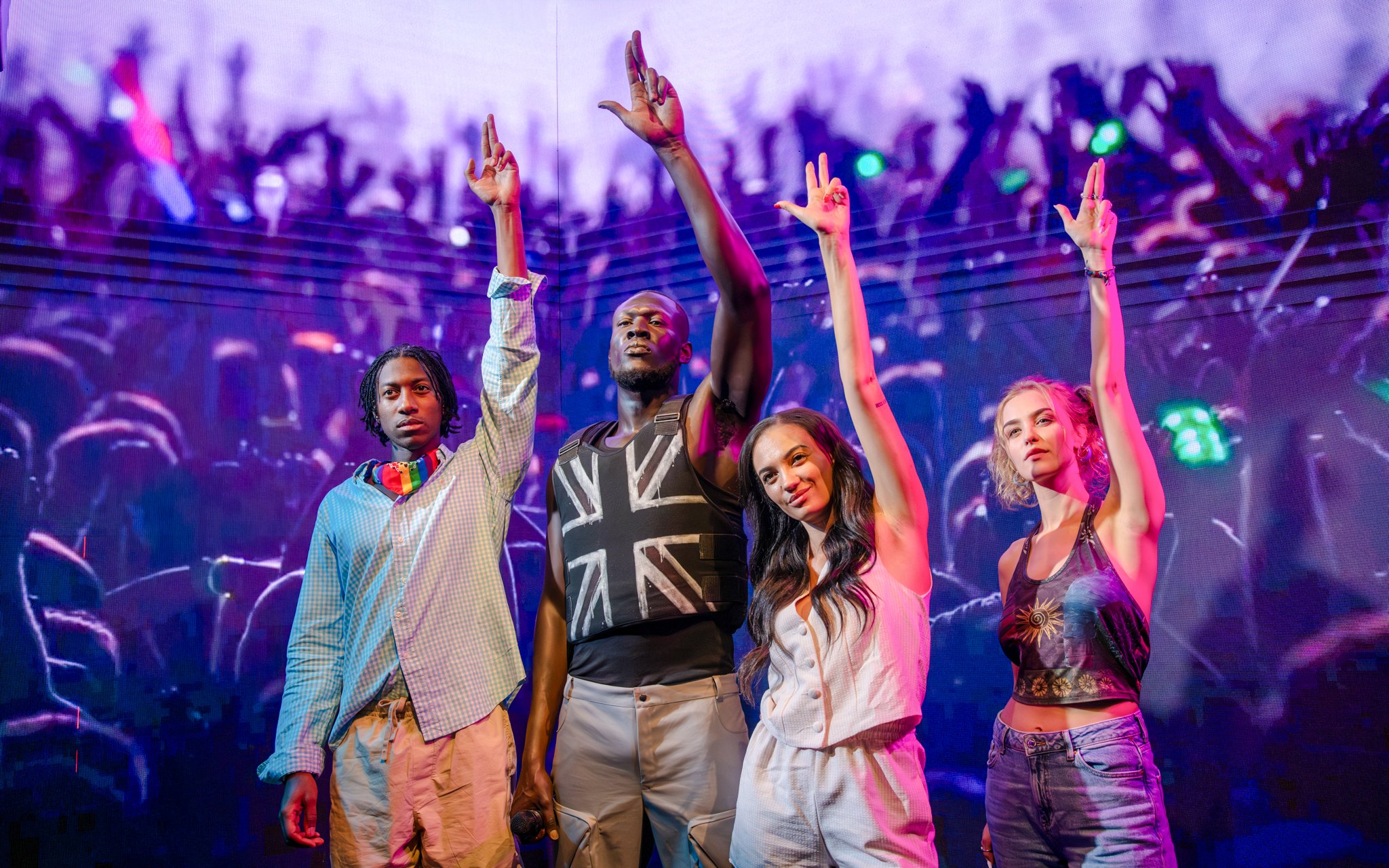 Wax figures of four people at Madame Tussauds London with a concert backdrop.