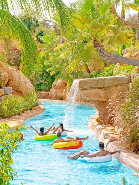 Lazy river with people on floats at Zoomarine Algarve surrounded by lush greenery.