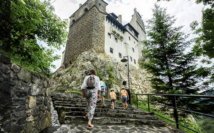 Tourists with children walking up stone steps to Bran Castle, Romania.