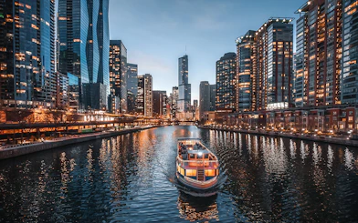 Cruise boat on Chicago River with city skyline at dusk.