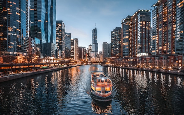 Cruise boat on Chicago River with city skyline at dusk.