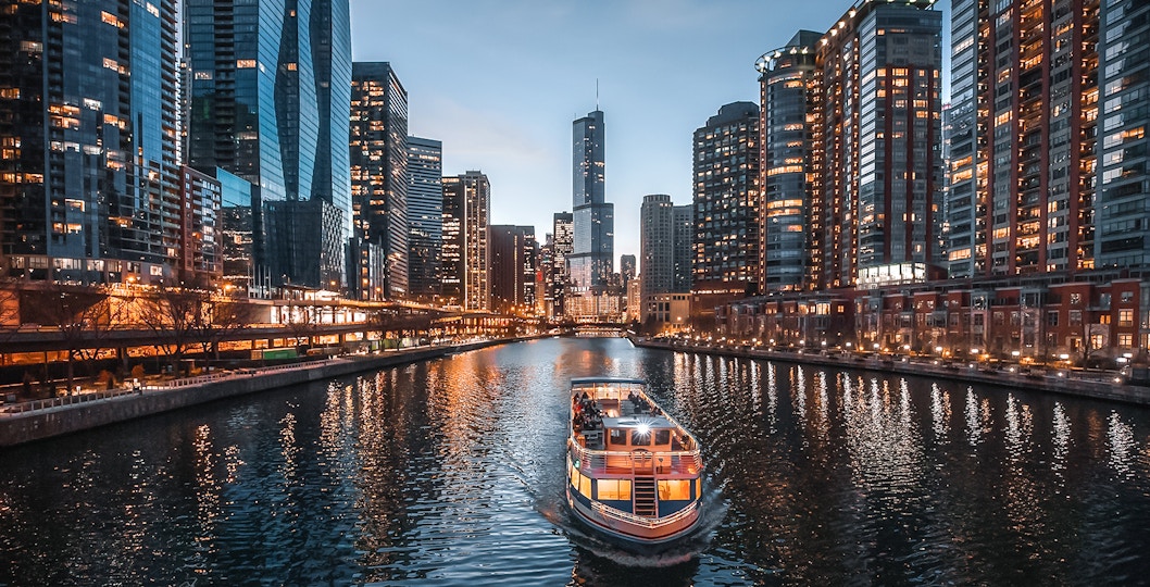 Cruise boat on Chicago River with city skyline at dusk.