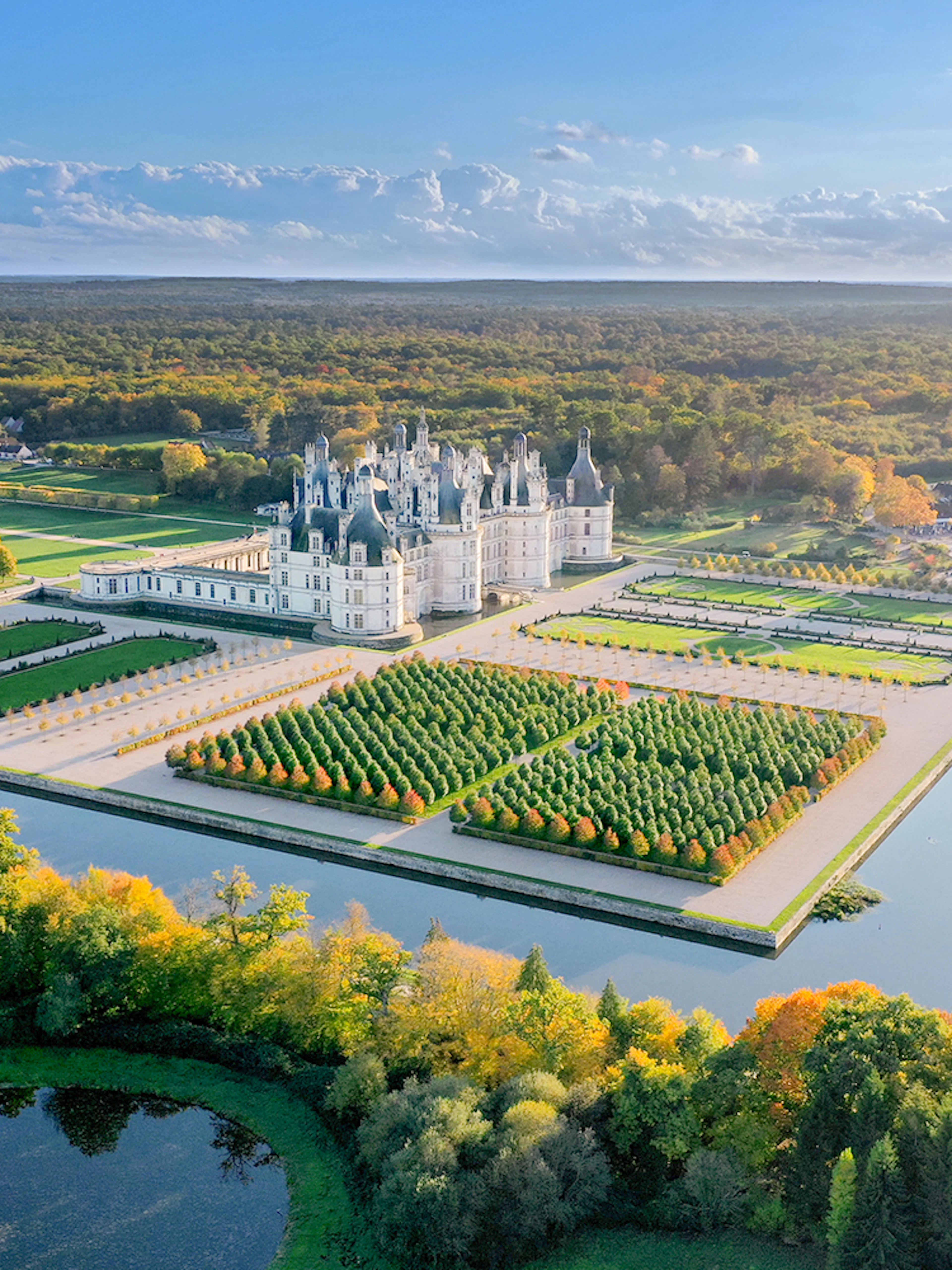 Chambord Castle and gardens aerial view, showcasing symmetrical landscaping and surrounding forest.